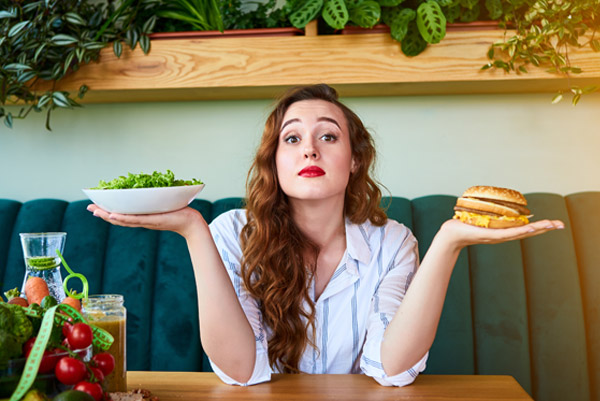 Mujer con un plato de ensalada en una mano y una hamburguesa en la otra
